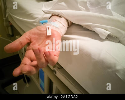 Soft focus mano della donna caucasica con una linea endovenosa (IV) sul letto in una clinica (Ospedale) Foto Stock