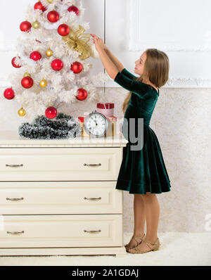 Giorno preferito dell'anno. Celebrazione della Messa di Natale. Ottenere incredibilmente entusiasti di natale. Kid ragazza nei pressi di albero di natale in attesa della mezzanotte orologio. Ultimi preparativi. Bambino festeggiano il Natale a casa. Foto Stock