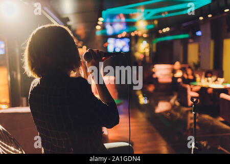 Giovane donna cantare in karaoke e tenendo un microfono di close-up. Cantante a un partito o a un concerto sullo sfondo di una stella luminosa e di fumo Foto Stock