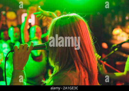 Giovane donna cantare in karaoke e tenendo un microfono di close-up. Cantante a un partito o a un concerto sullo sfondo di una stella luminosa e di fumo Foto Stock