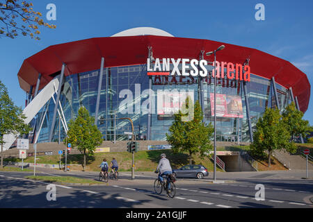 La Lanxess Arena, indoor arena multifunzione, con facciata di vetro rosso e rivestimento in alluminio e lunga span tetto supportato da bianco arco in acciaio fascio. Foto Stock