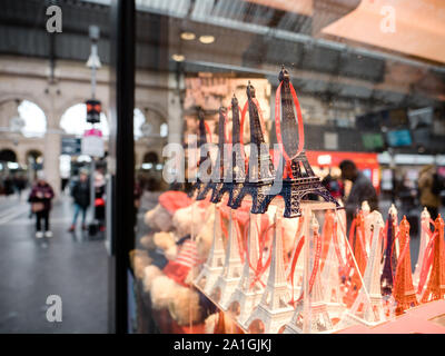 Parigi, Francia - Jan 20, 2019: più decorativo Torre Eiffel statue nelle vetrine del negozio di souvenir nel centro di Parigi con persone sagome in background Foto Stock