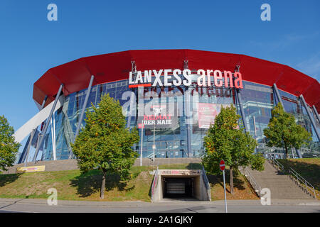 La Lanxess Arena, indoor arena multifunzione, con facciata di vetro rosso e rivestimento in alluminio e lunga span tetto supportato da bianco arco in acciaio fascio. Foto Stock