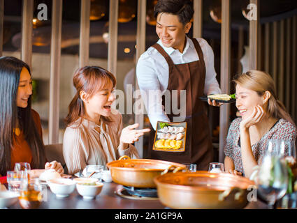 Cameriere portare gnocco di uovo per hot pot e che serve un gruppo di amici nel ristorante Foto Stock