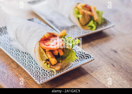 Gyros greco avvolto in un pane pita su uno sfondo di legno. La cucina greca concetto. Foto Stock