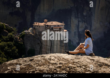 Tourist donna seduta sulla cima della montagna sulla bellissima scenic clif sfondo vicino Meteora monasteri in Grecia. Foto Stock