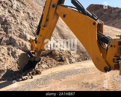 Il giallo del retroescavatore del caricatore scava una trincea durante la guida su strada con opere di costruzione. Movimento terra, scavi, scavando sui terreni rocciosi. Foto Stock