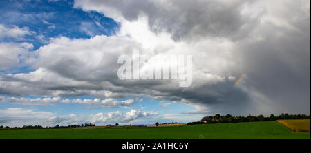 Rainbow su una verde e campo giallo con nuvole grigie nella drammatica caduta tempesta Foto Stock
