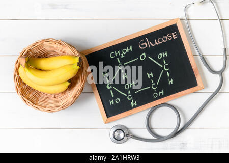 Molecola di glucosio su lavagna con banana e stetoscopio in legno su sfondo bianco, Dieta e scienze alimentari concetto Foto Stock