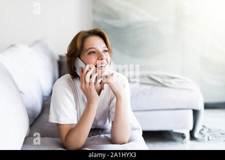 Giovani sorriso donna chiamata sul divano nel soggiorno, a casa - in ambienti chiusi, eccitato ragazza distesa parlando al cellulare Foto Stock