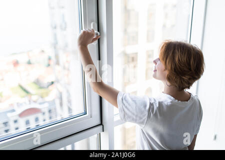 Giovane donna di apertura della finestra in salotto Foto Stock