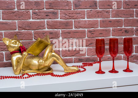 Golden cat leggendo un libro giace su una superficie bianca con perle di rosso e rosso bicchieri da vino, living room interior Foto Stock