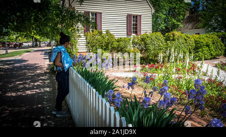 Donna Thai appoggiata contro white Picket Fence davanti a fiori colorati e tradizionale casa coloniale Foto Stock