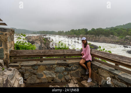 Donna in maglia rosa in piedi di fronte a correre acqua a Great Falls National Park in un tempestoso giorno nuvoloso Foto Stock