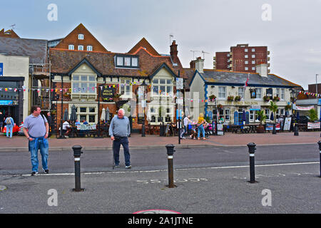 La gente seduta al di fuori del pub lungo il porto di Poole, compreso il Jolly Sailor e il Lord Nelson. Altri passeggiando lungo la strada. Foto Stock