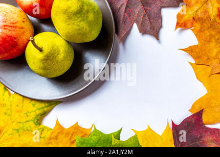 Autunno sfondo rosso con mele e pere giallo su una piastra marrone Circondato da colorati foglie di acero su uno sfondo bianco con la scritta aut Foto Stock