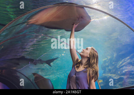 Una giovane donna tocca un pesce di razza in un tunnel oceanarium Foto Stock