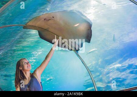 Una giovane donna tocca un pesce di razza in un tunnel oceanarium Foto Stock