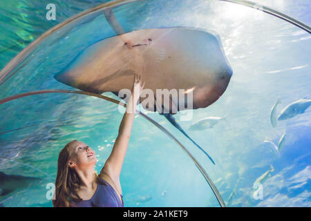 Una giovane donna tocca un pesce di razza in un tunnel oceanarium Foto Stock