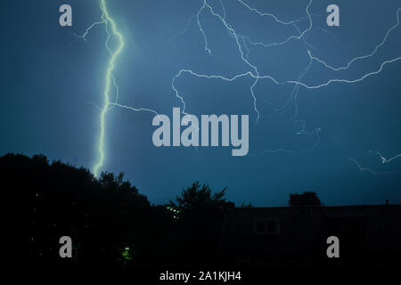 Un fulmine luminoso colpisce la terra di notte. Accanto a questo canale principale per i fulmini, molti piccoli canali per i fulmini possono essere visti in aria. Foto Stock