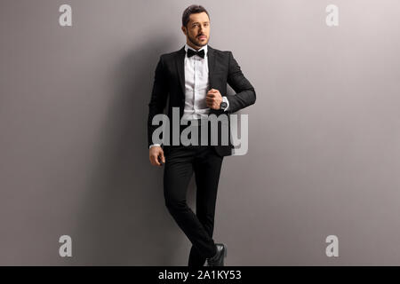 Elegante giovane uomo in un abito nero e il filtro bow tie appoggiato su di un muro grigio Foto Stock