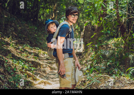 Il padre porta suo figlio in un bambino che porta è escursionismo nella foresta. Tourist sta portando un bambino sulla sua schiena nella natura del Vietnam Foto Stock