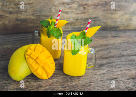 Frullato succoso di mango in due vasetti di vetro in muratura con paglia rossa a righe su vecchio sfondo di legno. Concetto di vita sana, spazio di copia Foto Stock
