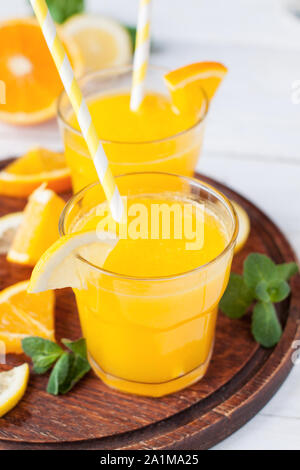 Due bicchieri di agrumi rinfrescanti drink con spicchi di limone e arancio e foglie di menta sul tagliere di legno Foto Stock