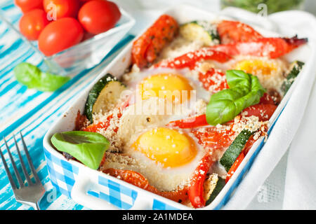 Uova al forno con zucchinii, basilico, cipolla, peperone, pomodori. Una sana prima colazione Foto Stock