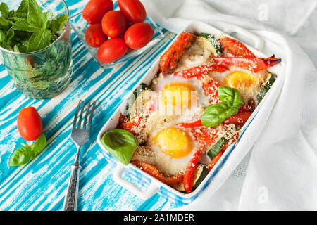 Uova al forno con zucchinii, basilico, cipolla, peperone, pomodori. Una sana prima colazione Foto Stock