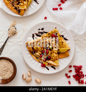 Crespelle sottili con il cioccolato fuso, i semi di sesamo, melograno e mandorle Foto Stock