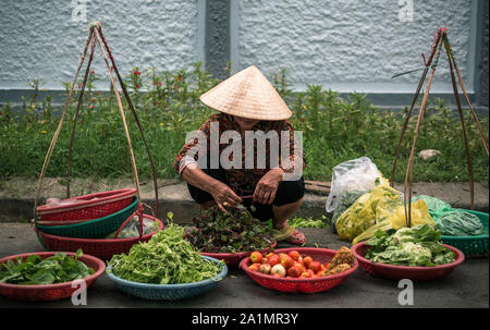 Femmina strada vietnamita fornitore con cappello conico la vendita di frutta e verdura di Hue street market, tonalità, Vietnam Foto Stock