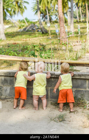 Tre bambini che guardano attraverso la recinzione sulle galline e i galli nel capannone. Le camicie gialle. Foto Stock