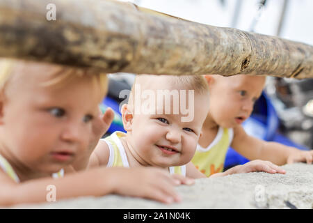 Tre bambini che guardano attraverso la recinzione sulle galline e i galli nel capannone. Le camicie gialle. Foto Stock