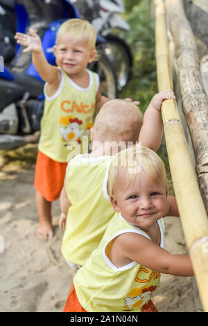 Tre bambini che guardano attraverso la recinzione sulle galline e i galli nel capannone. Le camicie gialle. Foto Stock