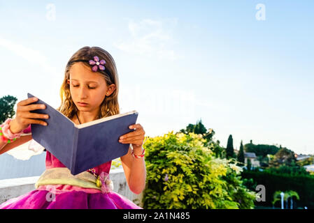 Bambina vestita come una principessa la lettura di una storia, favorendo l'immaginazione. Foto Stock