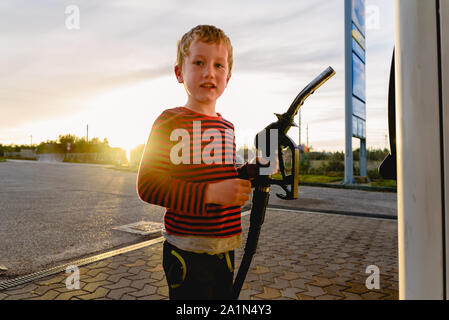 Bambino tenere il tubo di una pompa del carburante al tramonto in corrispondenza di una stazione di gas. Foto Stock