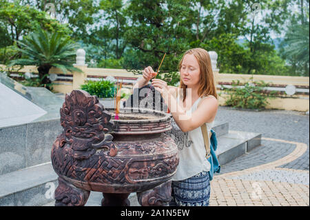 Giovane donna Traveler che prega in un'azione educata con bastoncini d'incenso Al tempio buddismo in Vietnam Foto Stock