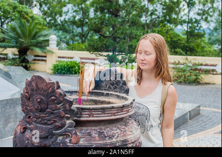 Giovane donna Traveler che prega in un'azione educata con bastoncini d'incenso Al tempio buddismo in Vietnam Foto Stock