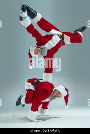 Felice Natale Santa Claus su grigio di sfondo per studio. Caucasica modello maschile in vacanza tradizionale costume del. Concetto di vacanze, Capodanno, umore invernale, doni. Jumping, rendendo trucchi. Copyspace. Foto Stock