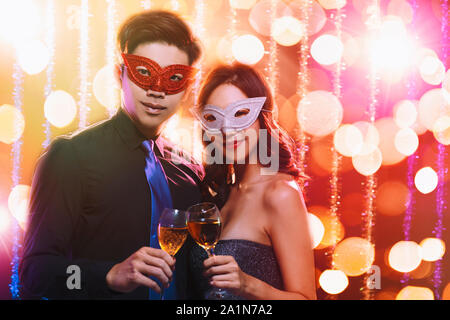 Coppia giovane per celebrare il nuovo anno e di bere champagne su masquerade party Foto Stock