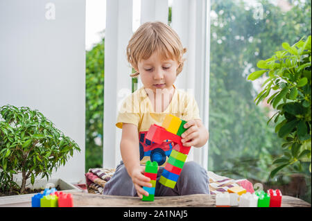 Piccolo ragazzo carino con giocare con un sacco di blocchi di plastica colorati al coperto. Bambino attivo che si diverte con la costruzione e la creazione di torre. Promozione Foto Stock