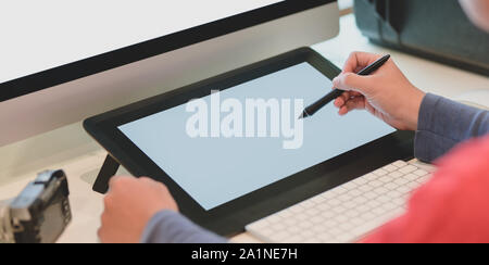 Vista ravvicinata del giovane maschio fotografo modifica le sue immagini su tavoletta digitale nel suo posto di lavoro Foto Stock