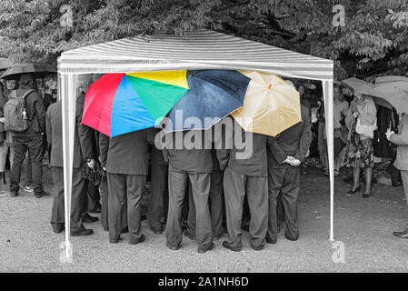 Un gruppo di uomini in abito scuro sotto ombrellone Foto Stock