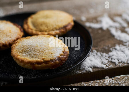 Tre tritare la torta su un piatto nero su una tavola in legno rustico con la neve Foto Stock