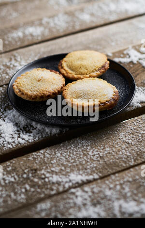 Tre tritare la torta su un piatto nero su una tavola in legno rustico con la neve Foto Stock