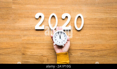 2020 Celebrazione conto alla rovescia con mano che tiene sveglia e mock up numero di testo sulla tavola di legno Foto Stock