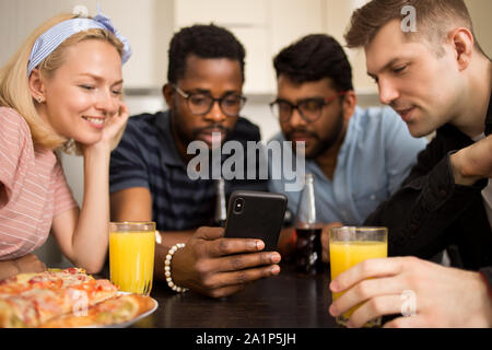 Gli amici utilizzando gadget durante il pranzo di mangiare la pizza, guardare video sullo smartphone, la lettura di social media posti, rendendo la chiamata video, seduti insieme a tabl Foto Stock