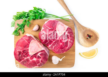 Ossobuco di vitello con gambi di prezzemolo, limone e aglio per un gremolata, tipici italiani cucina lombarda ingredienti, flay giacciono su uno sfondo bianco Foto Stock