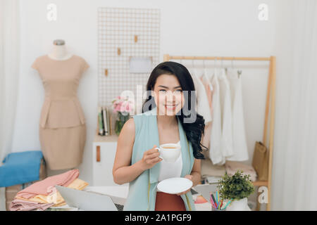 Ritratto di giovane e bella asiatica di designer di moda imprenditrice al suo studio mentre si beve il caffè Foto Stock